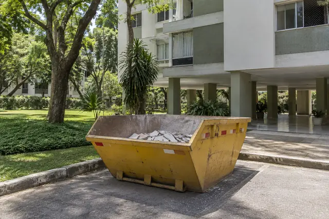 Aluguel de caçamba de entulho DF: caçamba para reforma junto a um bloco residencial sobre pilotis. Cena ilustrativa.