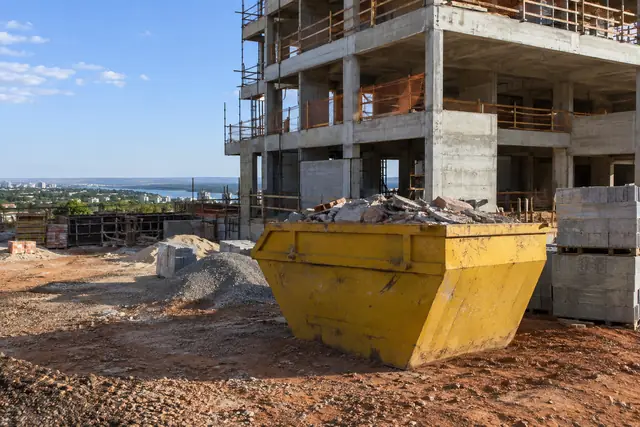 Aluguel de caçamba de entulho DF: caçamba em canteiro de construção de edifício — serviço disponível em Guará. Cena ilustrativa.